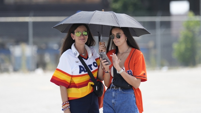 Two women use umbrella to shade themselves from the sun.
