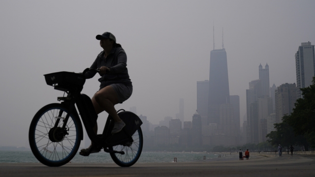 A person rides a bicycle along the shore of Lake Michigan as the downtown skyline is blanketed in haze.