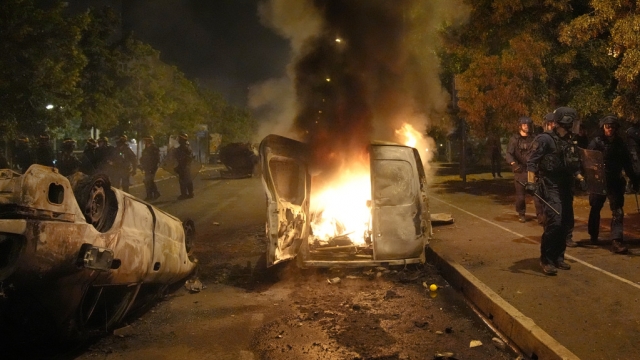 Police officers walk past burning cars near Paris.