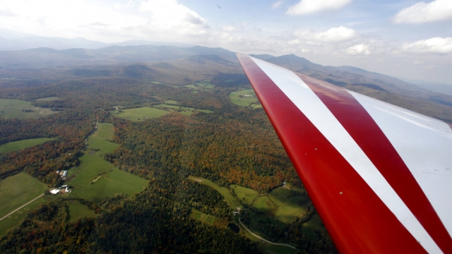 A plane wing soars above rural lands