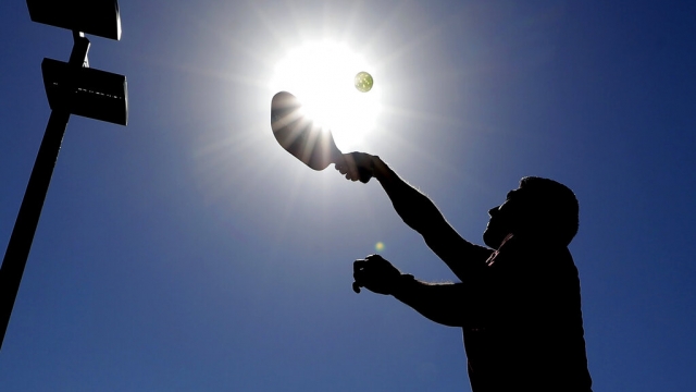 The silhouette of a pickleball player against a sunny sky.