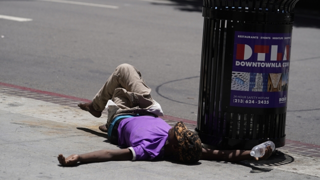 A person lies on the sidewalk in Los Angeles heat.