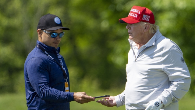 Walt Nauta, left, takes a phone from Former President Donald Trump during the LIV Golf Pro-Am.