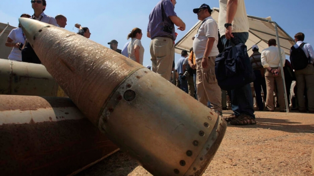 Activists and international delegations stand next to cluster bomb units.