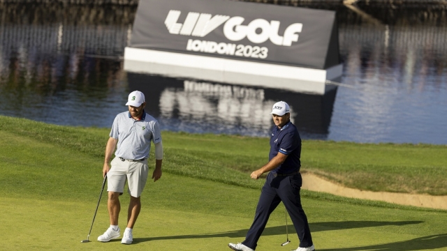 Professional golfers Louis Oosthuizen and Patrick Reed on a golf course with an LIV Golf sign in the background.