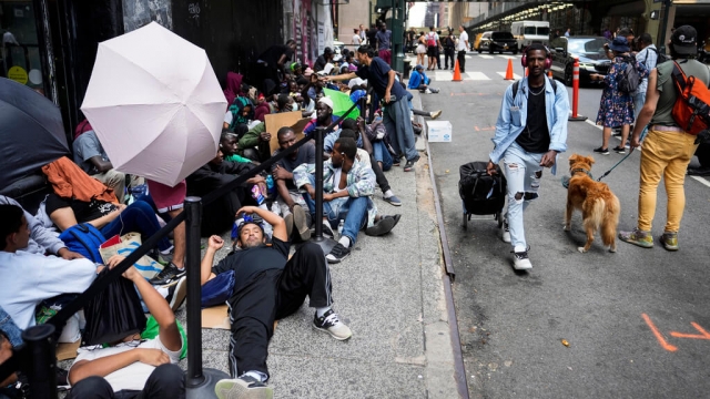 Migrants sit in a queue outside of The Roosevelt Hotel.