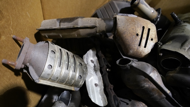 Used catalytic converters removed from cars at a salvage yard piled up in a carton.