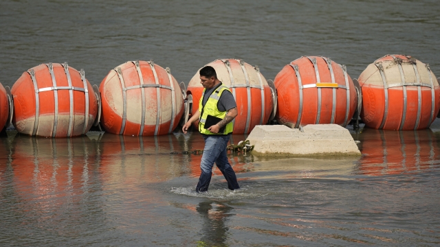 A worker inspects buoys being used as a barrier along the Rio Grande.