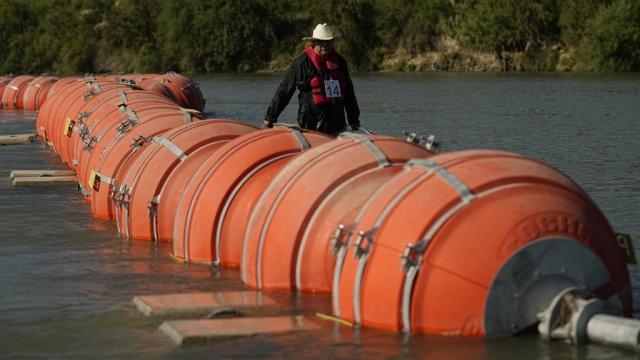 A kayaker walks past large buoys being used as a floating border barrier on the Rio Grande.