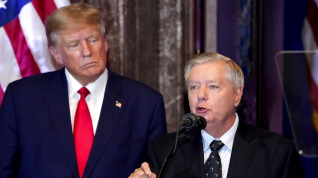 Former President Donald Trump listens as Sen. Lindsey Graham, R-S.C., speaks at a campaign event.