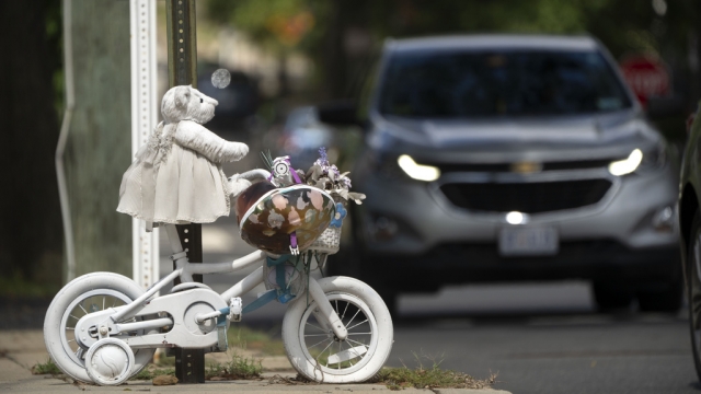 A vehicle drives past a memorial for a girl who was struck and killed by a driver.