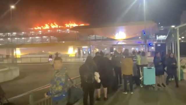 People stand in front of a building on fire.