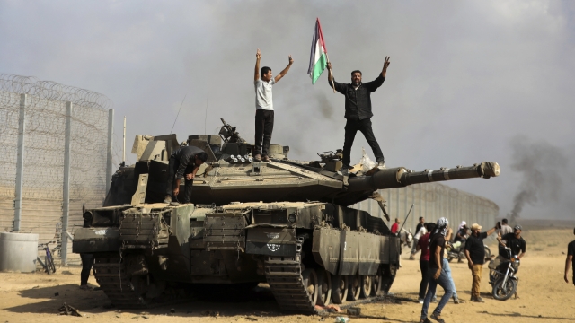Palestinians wave their national flag and celebrate by a destroyed Israeli tank at the Gaza Strip