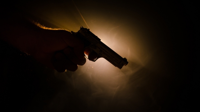 Person holding gun with a dark background.