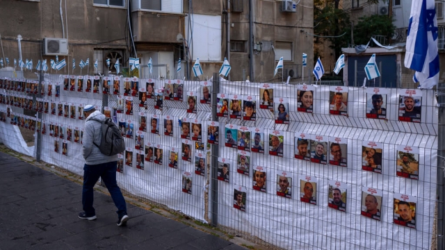 A man passes by a fence with photographs of hostages, mostly Israeli civilians.