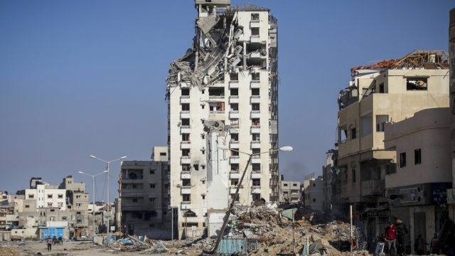 Palestinians walk by destroyed buildings in Gaza City.