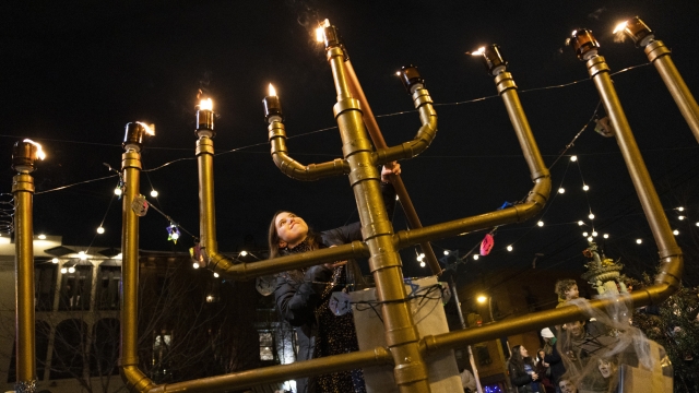 A woman lights a menorah during a public Hanukkah celebration
