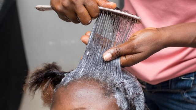 Stylist applying relaxer cream with a comb to natural long hair.