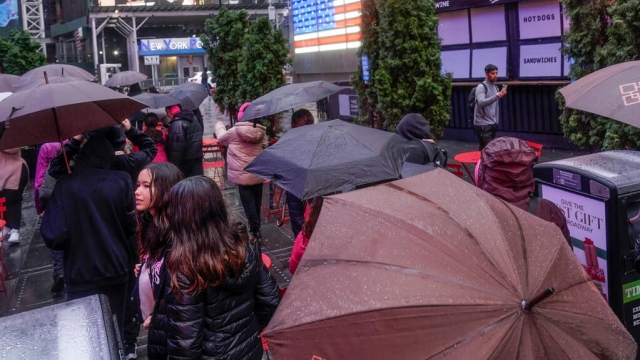 Pedestrians take cover under umbrellas as they walk through a wet Times Square in New York, Monday, Dec. 18, 2023