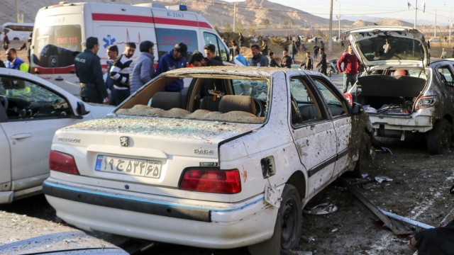 People stay next to destroyed cars after an explosion in Kerman, Iran