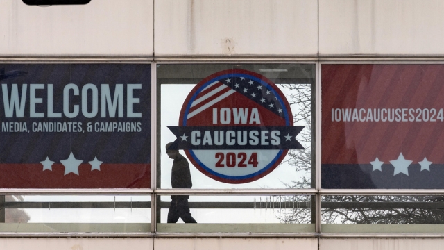 A man walks past a sign that reads "Iowa Caucuses 2024."