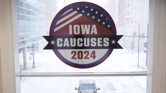 A pickup truck is driven down a snow covered road under an Iowa Caucus sign.