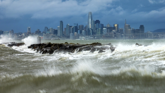 Waves crash over a breakwater in Alameda, Calif., with the San Francisco skyline in the background on Sunday, Feb. 4, 2024.