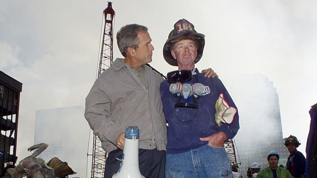 President George W. Bush, left, stands with New York City firefighter Bob Beckwith on a burnt fire truck.