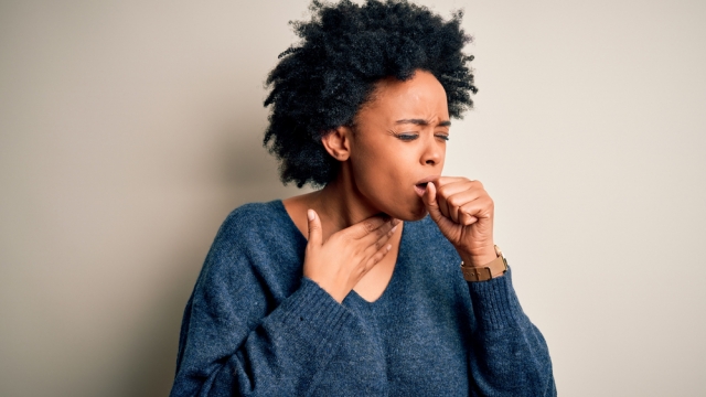 Young woman coughing with her hand to her throat area.