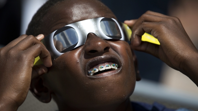 A young boy holds solar eclipse glasses to his eyes.