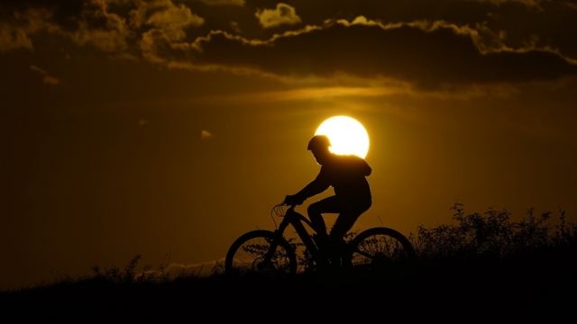 A cyclist tops a hill on a hot day at sunset, Aug. 20, 2023, in San Antonio.
