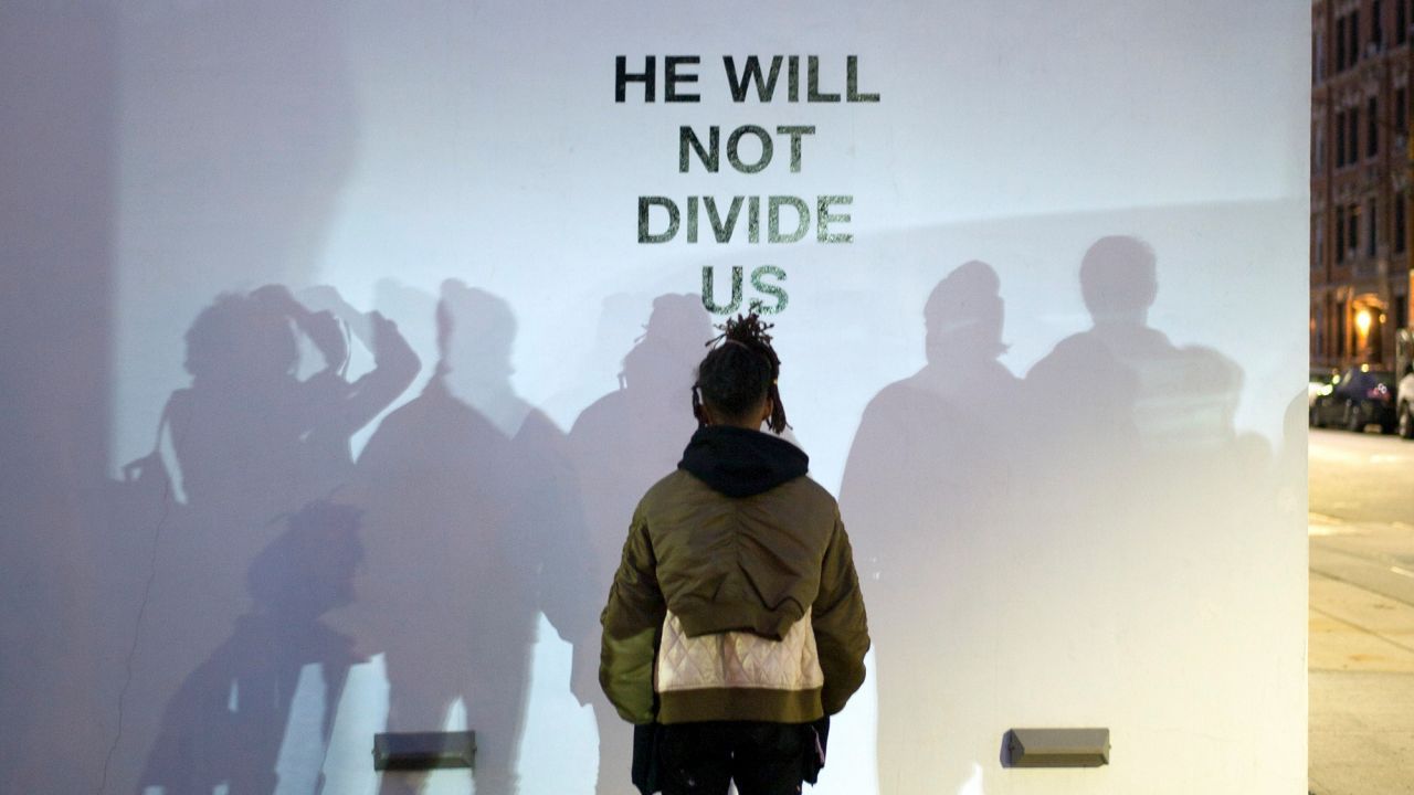 Jaden Smith faces a wall with the words "he will not divide us" printed on it.