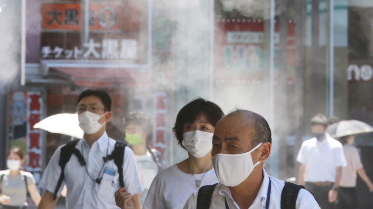 People wearing face masks to protect against the spread of the coronavirus walk under a water mist in Tokyo