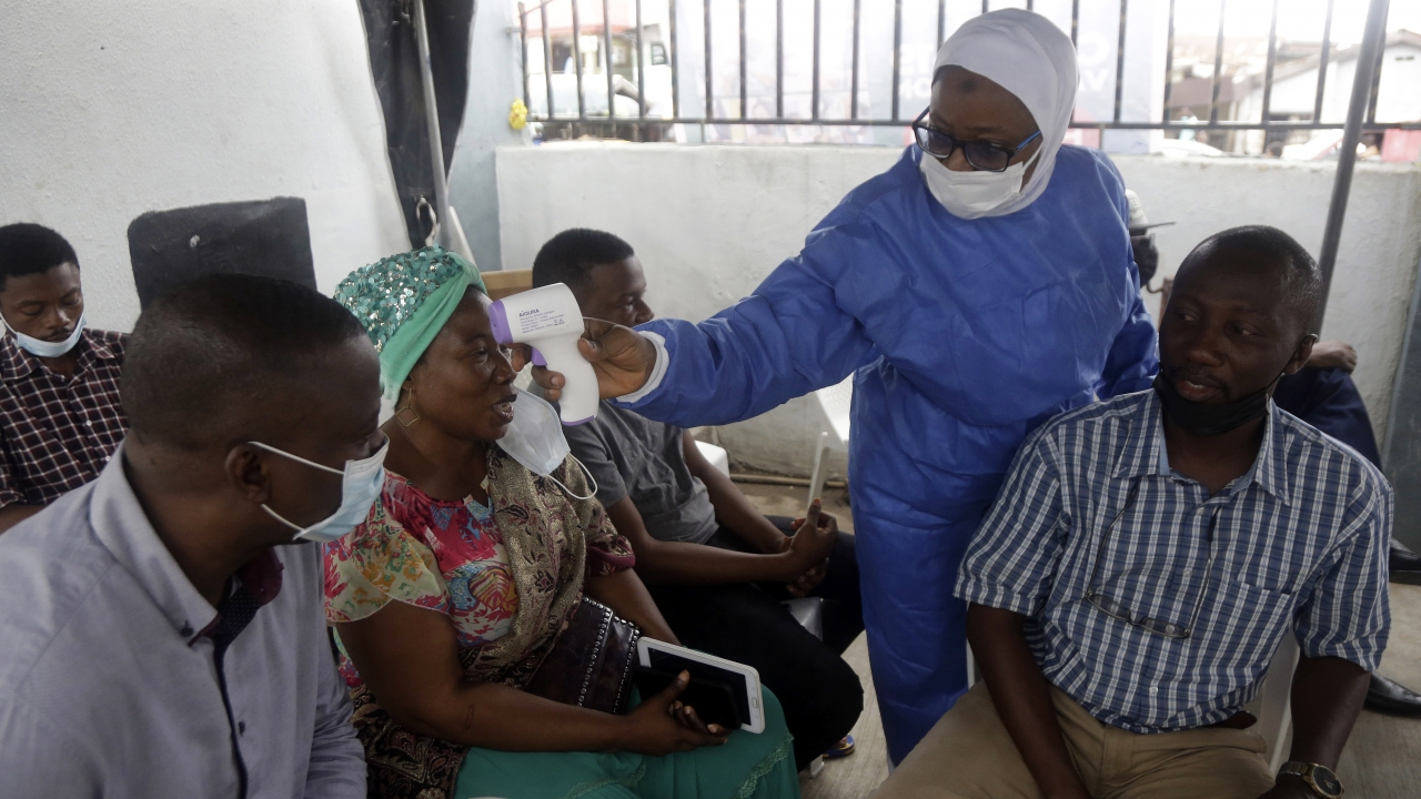 A nurse in protective gear, center, takes temperature of people waiting to take the Moderna coronavirus vaccine