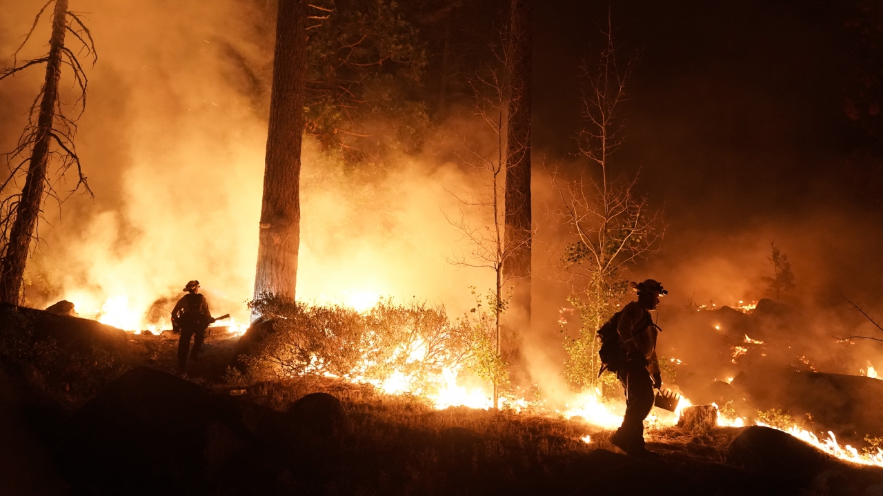 Two firefighters monitor the Caldor Fire burning near homes in South Lake Tahoe, Calif.