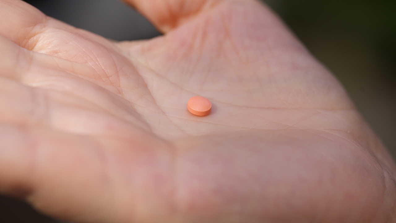 A woman holds an aspirin pill in her hand.