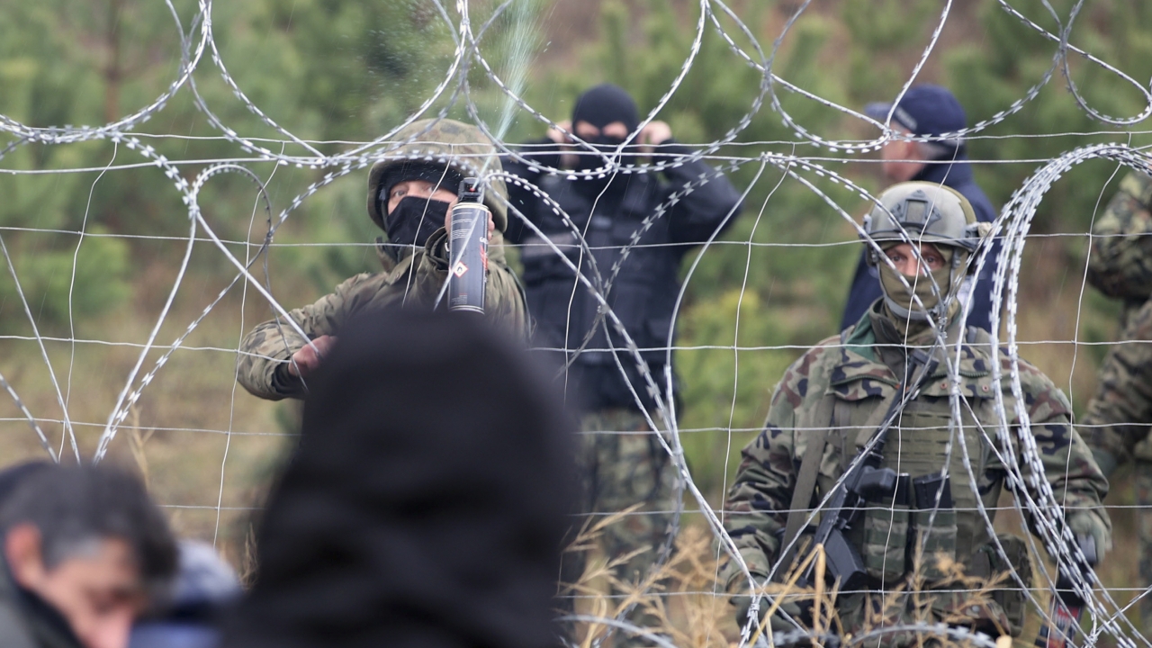 A photo of Polish border guards standing near barbed wire as mirgants seek to enter.
