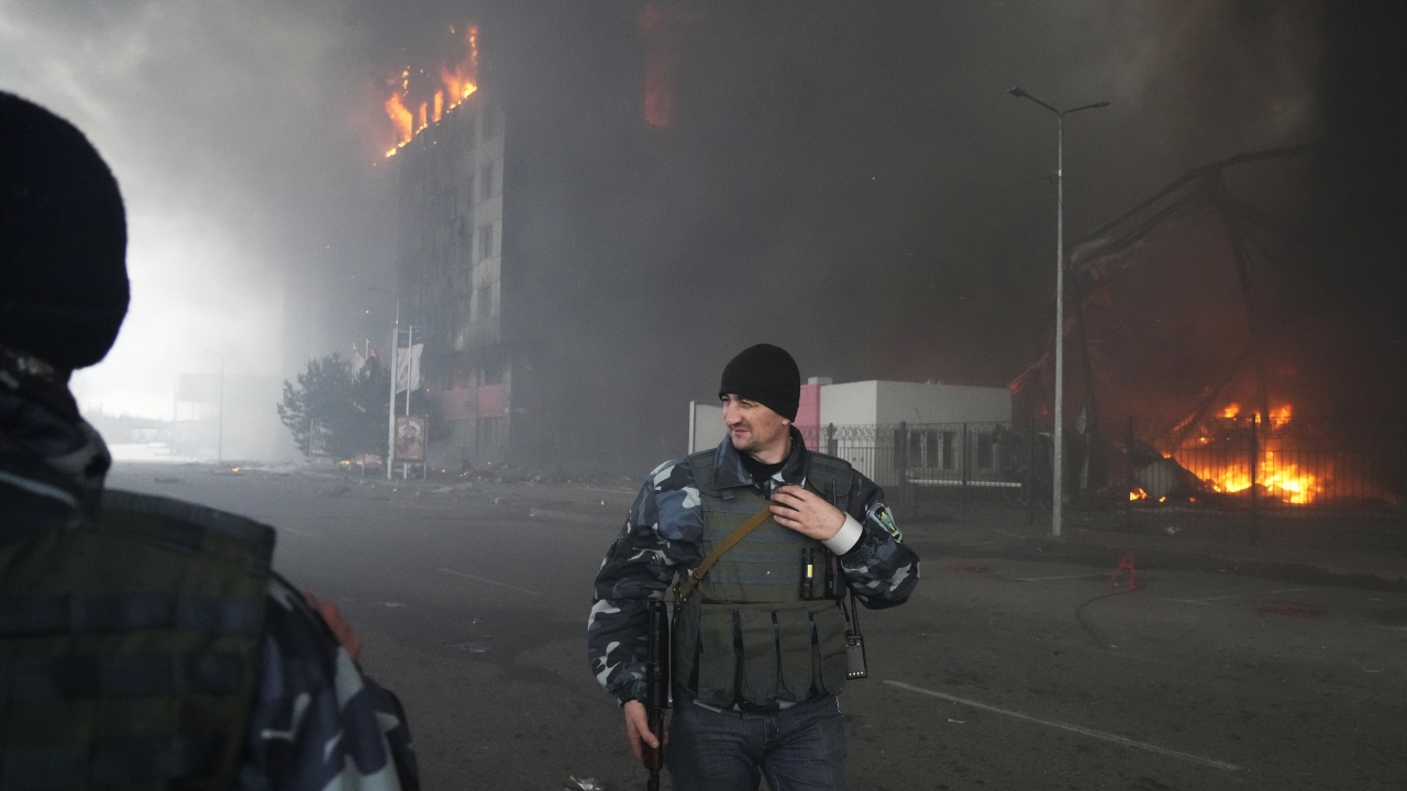 Ukrainian servicemen walk as fire and smoke rise over a building.