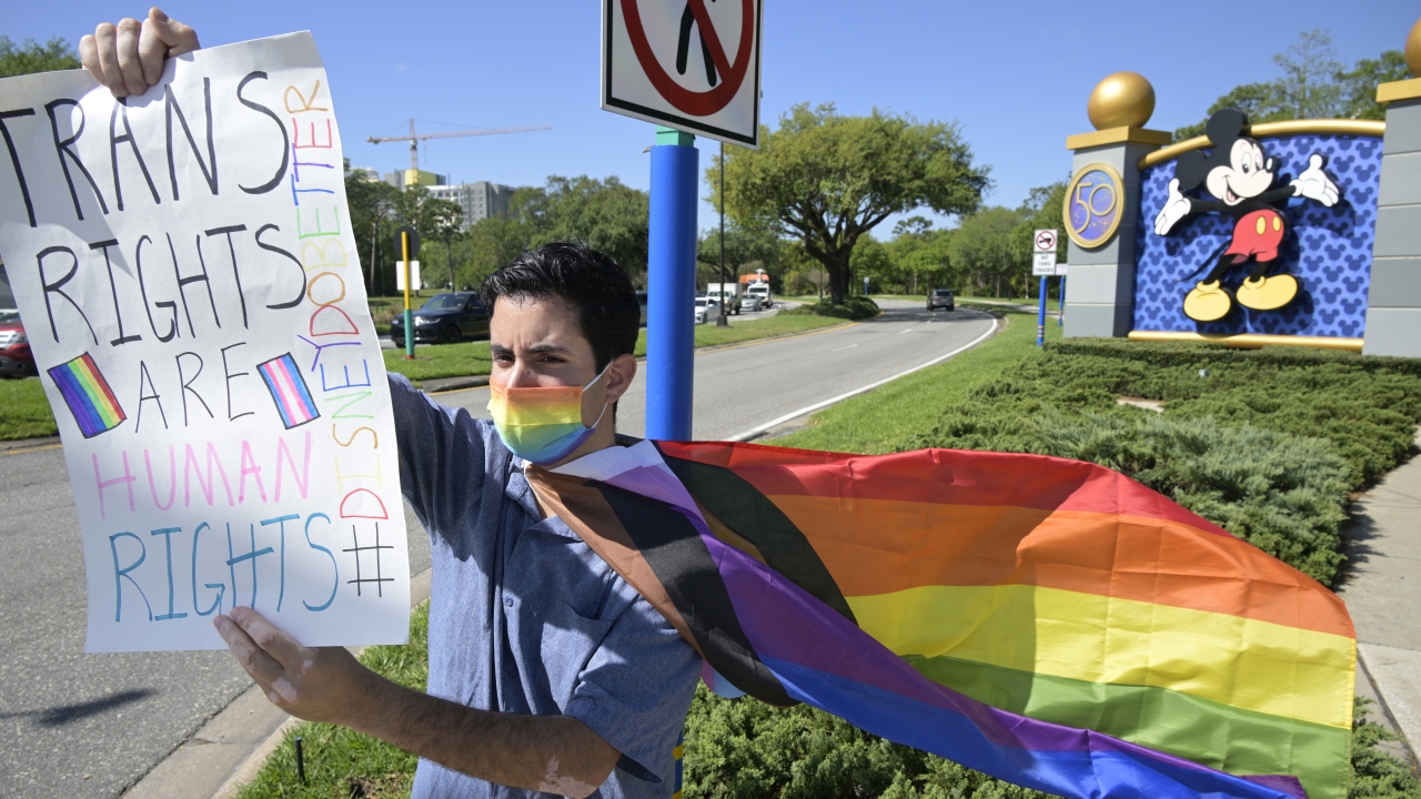 A Disney cast member protests his company's stance on LGBTQ issues while holding a sign supporting trans rights