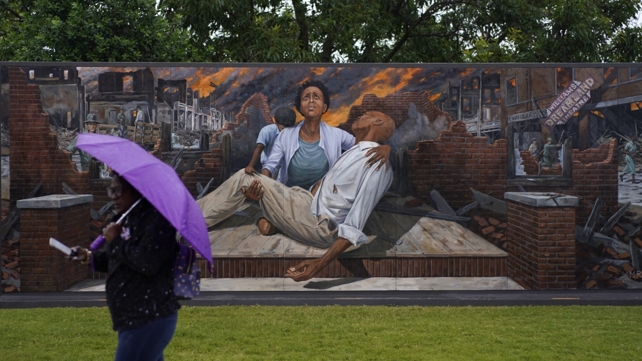 A woman walks by a mural depicting the Tulsa Race Massacre
