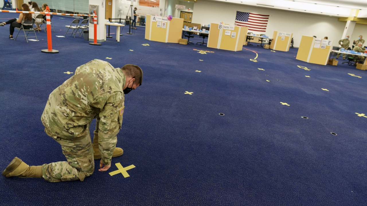 An Army National Guard member pulls up tape marking a line at a coronavirus mass-vaccination site