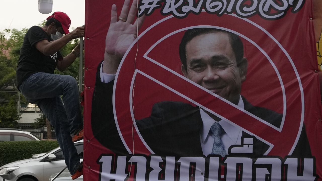 An anti-government protester climbs on a car beside a poster of Prime Minister Prayuth Chan-ocha.