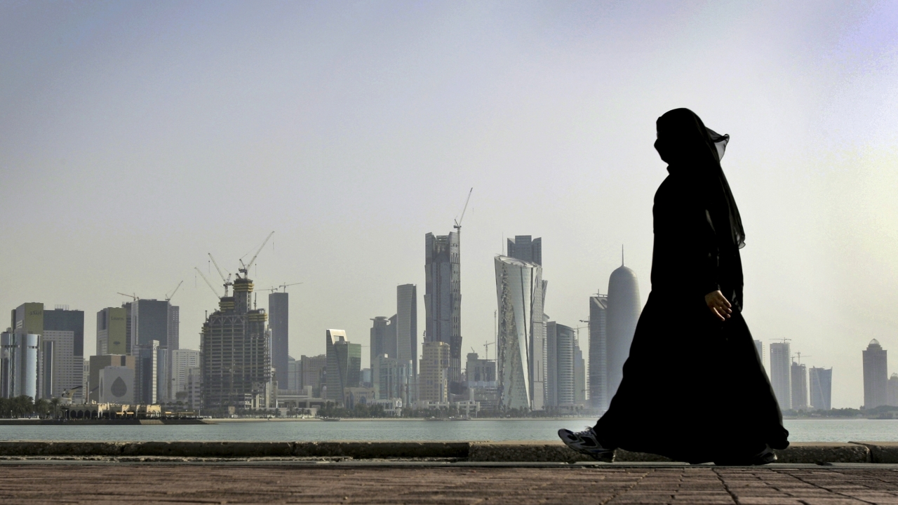 A Qatari woman walks in front of the city skyline in Doha, Qatar