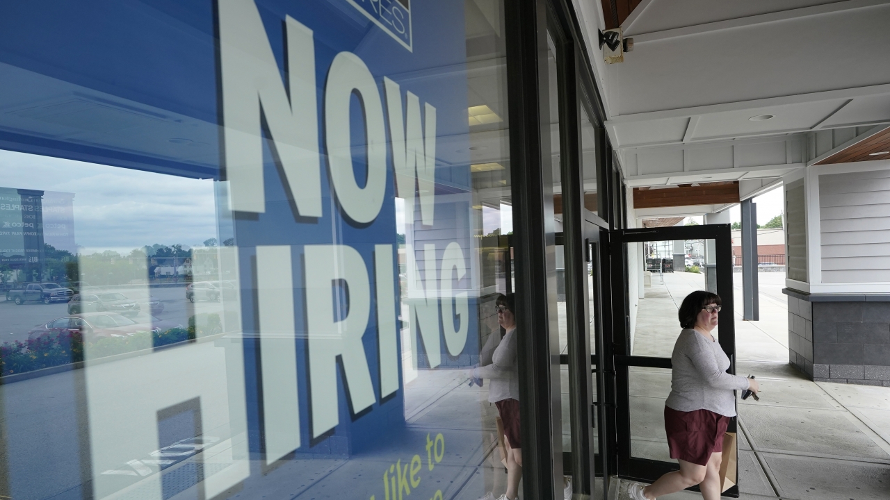 A woman passes a hiring sign in front of a business.