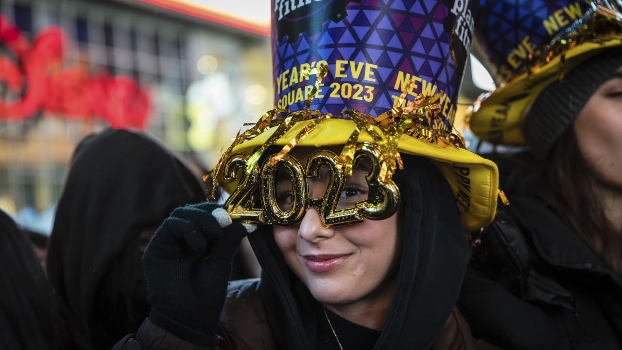 A woman wears a sponsor hat and 2023 fashioned glasses in New York's Times Square