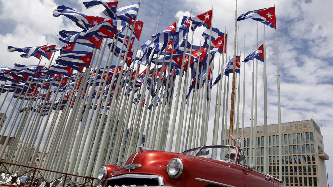 A classic American convertible car passes beside the U.S. embassy as Cuban flags fly at the Anti-Imperialist Tribune
