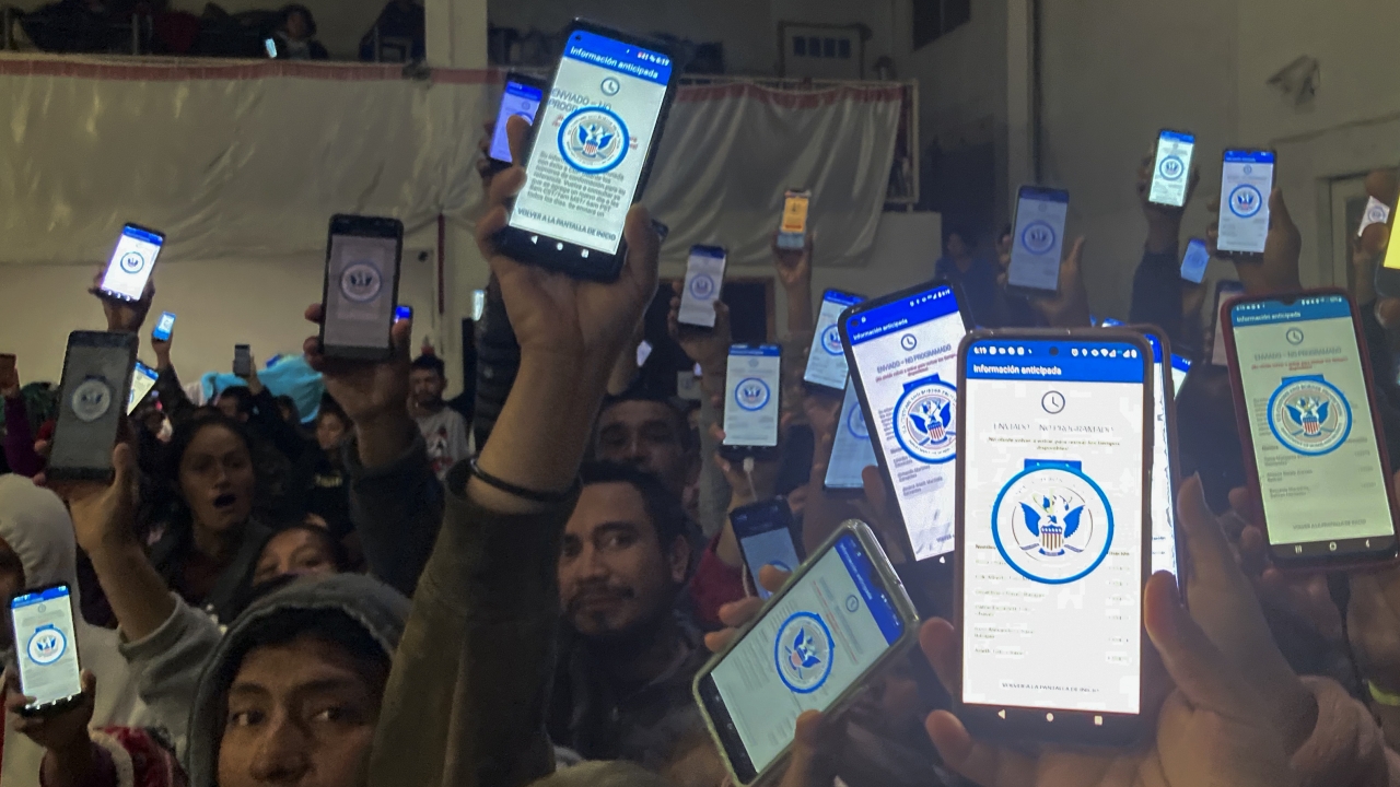 Migrants hold up their phones showing the CBPOne app.