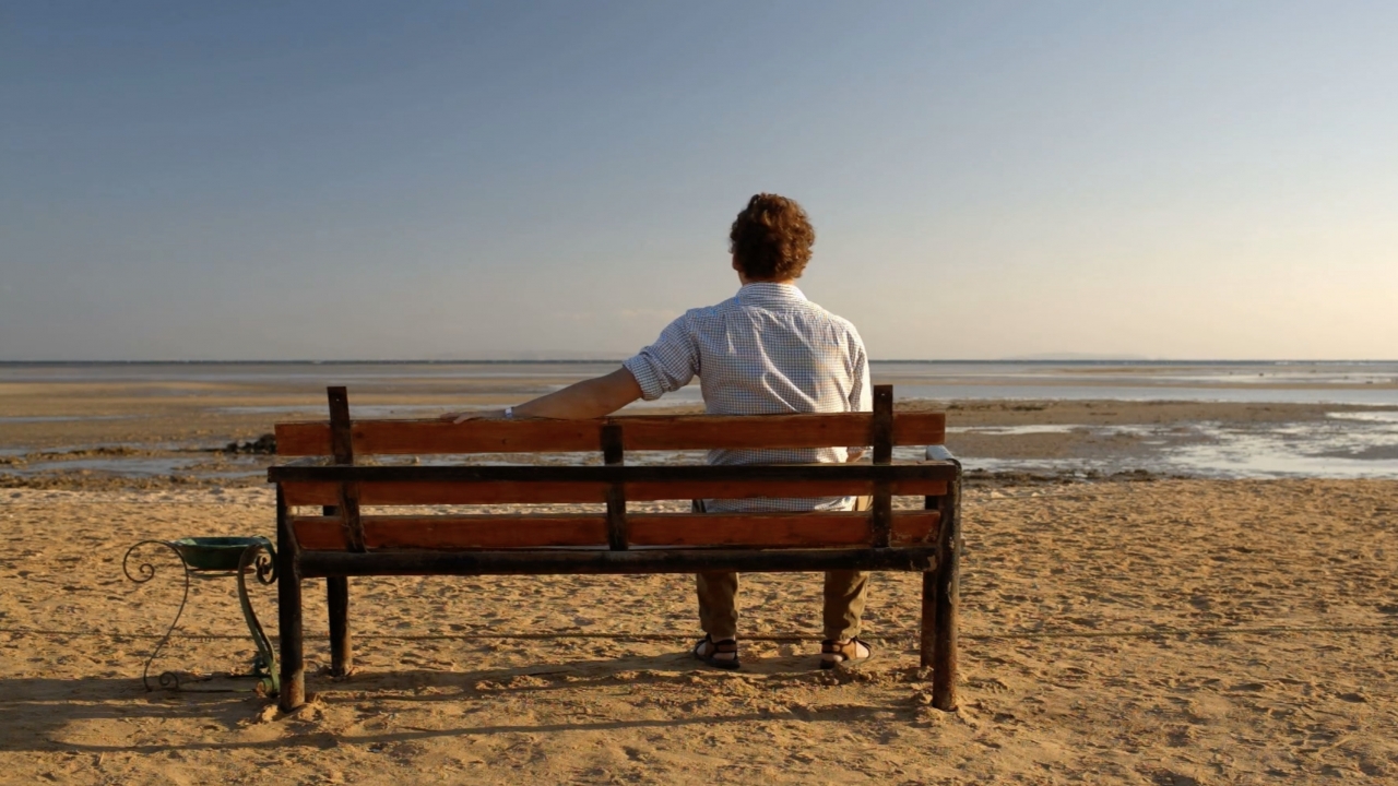 Man sitting alone on a bench at the beach.