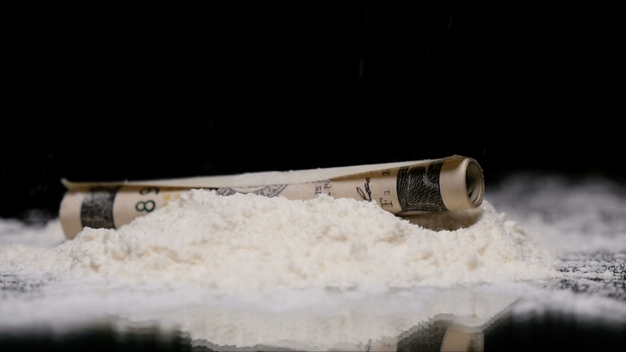 A rolled up dollar bill sits in a pile of cocaine.