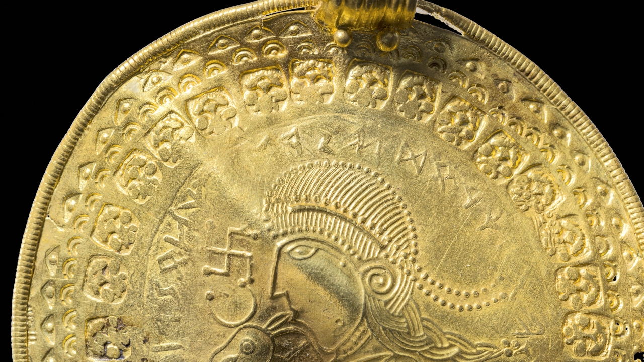 The inscription ‘He is Odin’s man’ is seen in a round half circle over the head of a figure on a golden bracteate.